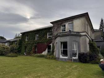 Eine großzügige Villa mit einem gepflegten Rasen und einem bewachsenen Fassadengrün.
