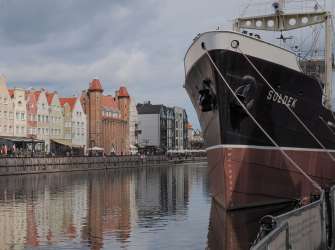 Das Bild zeigt ein Schiff namens "Sołdek", das in einem Hafen vor einer Reihe bunter Gebäude liegt.