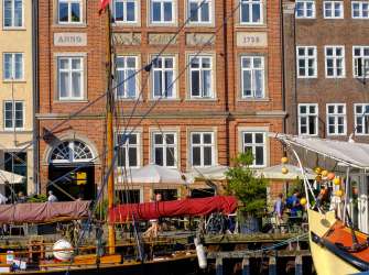 An einem sonnigen Tag liegt ein Segelschiff vor einer Reihe historischer Gebäude in einem Hafen.