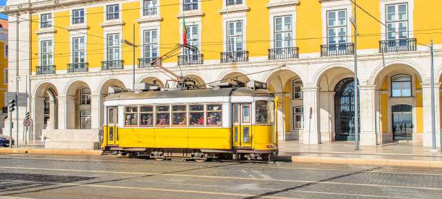 Histroische Straßenbahn in Lissabon Eine gelbe Straßenbahn fährt vor einem großen gelben Gebäude