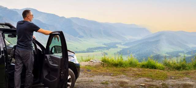 Ein mann steht neben seinem auto und schaut auf die berge