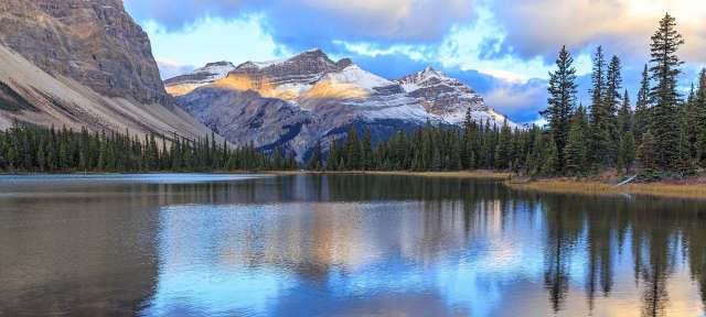 Den Sonnenaufgang genießen: Bow Lake Ein See mit Bergen im Hintergrund und Bäumen im Vordergrund