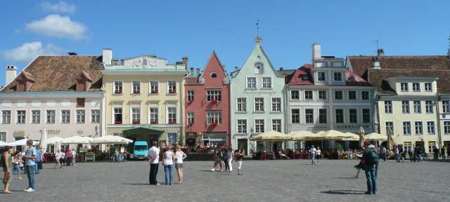 Tallinn: Rathausplatz – ©Alex Schoch Eine Gruppe von Menschen steht auf einem gepflasterten Platz in der Nähe einer Reihe von Gebäuden