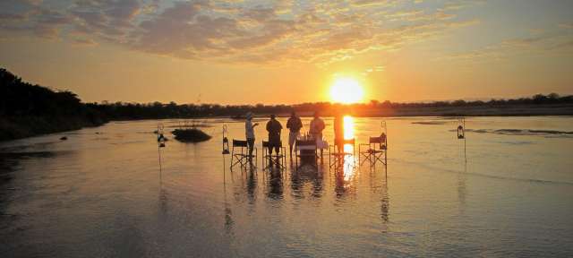 ©Dennis Eine Gruppe von Menschen steht in einem Fluss bei Sonnenuntergang