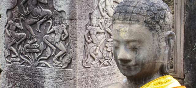 Eine buddhistische Statue steht vor einem Steinrelief