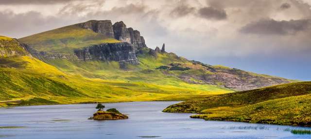 Old Man of Storr - Skye Ein See mit kleinen Inseln in der Mitte und einem Berg im Hintergrund
