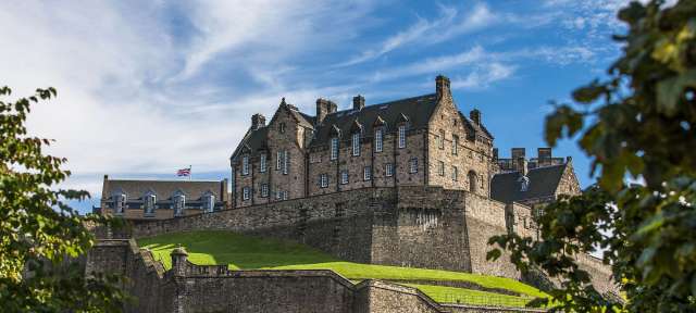 Edinburgh Castle Ein großes Gebäude auf einem Hügel mit einer Flagge darauf
