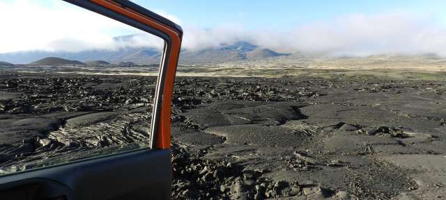 Saddle Road Big Island: Reisefoto von – ©Elke Metternich, Umfulana Ein orangefarbener jeep fährt durch ein felsiges feld