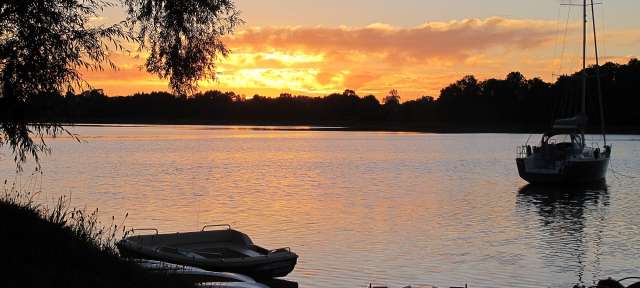 Masurische Seenplatte: Laschmiedensee – ©Martin Bach Ein Sonnenuntergang über einem See mit Booten im Vordergrund