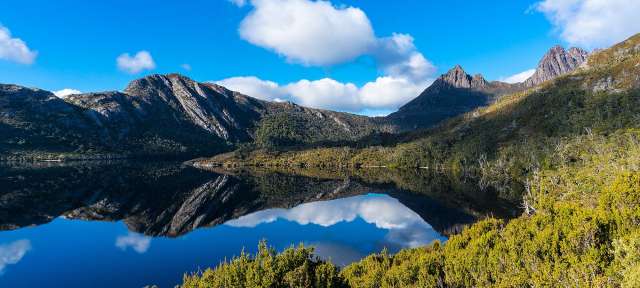 Ein See mit Bergen im Hintergrund und einem blauen Himmel mit Wolken