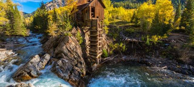 Ein Wasserrad steht auf einem Felsen neben einem Fluss