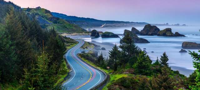 Einsam und romantisch: Küstenstraße 101 in Oregon Eine kurvenreiche Straße mit Bäumen und Felsen in der Nähe des Ozeans