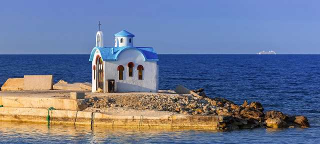 Eine kleine weiße und blaue Kirche sitzt auf einer kleinen Insel im Ozean