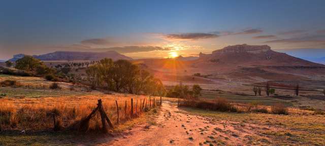 Weites Land: Burenland im Free State Ein Feldweg mit einem Zaun und einem Sonnenuntergang im Hintergrund
