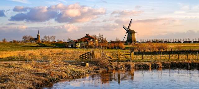 Eine Windmühle steht in einem Feld neben einem Fluss