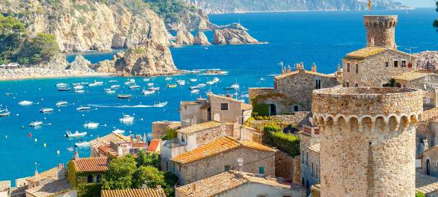 Tossa de Mar Eine Stadt mit einem Turm und vielen Booten im Hintergrund