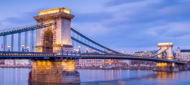 Kettenbrücke in Budapest Eine Brücke über einen Fluss mit einem Gebäude im Hintergrund