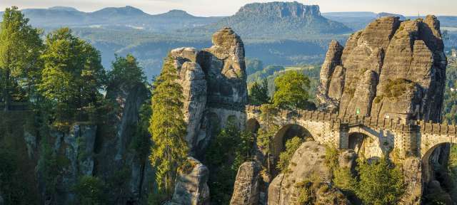 Sächsische Schweiz Eine Brücke zwischen zwei Felsen in einem Tal mit Bergen im Hintergrund