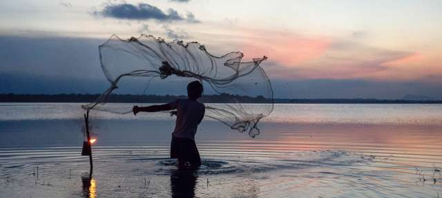 Ein Mann wirft ein Fischernetz in einen See