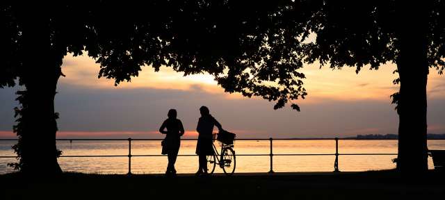 Bei Bregenz am Bodensee Eine Frau steht neben einem Mann mit einem Fahrrad bei Sonnenuntergang