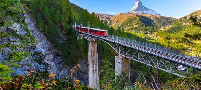 Ein roter Zug fährt auf einer Brücke mit einem Berg im Hintergrund