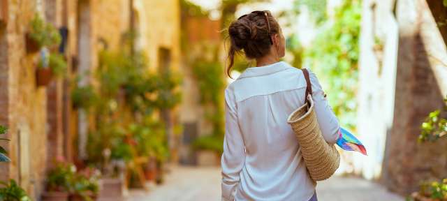 Eine Frau trägt einen Korb und geht eine schmale Straße entlang