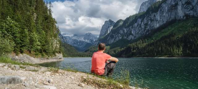 Ein Mann sitzt am Ufer eines Sees mit Bergen im Hintergrund
