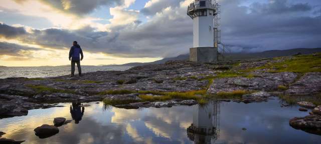 Sonnenuntergang in den schottischen Highlands Ein Mann steht vor einem Leuchtturm und schaut auf das Meer