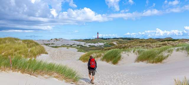 Weite, Ruhe und ein bekannter Leuchtturm: Amrum Ein Mann mit einem roten Rucksack geht durch die Dünen