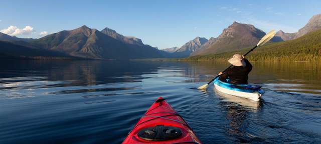 Aktiv auf Reisen: Kajakfahren in Alberta, Kanada Eine Person paddelt in einem Kajak auf einem See mit Bergen im Hintergrund