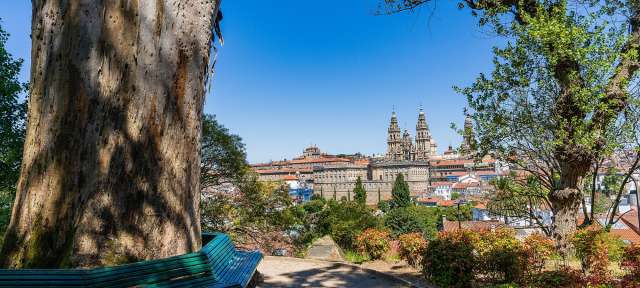 Ziel des Jakobswegs: Santiago di Compostela Eine Bank sitzt unter einem Baum mit einer Stadt im Hintergrund