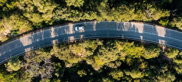 Elektroauto unterwegs Ein weißes Auto fährt auf einer kurvigen Straße durch einen Wald