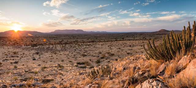 Endlose Weite: Kalahari Ein Sonnenuntergang in der Wüste mit Bergen im Hintergrund