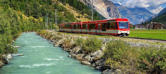 Ein rot-weißer Zug fährt an einem Fluss entlang