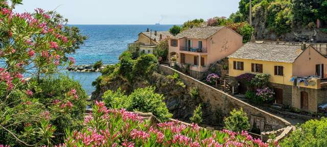Dorf Porticciolo in Cap Corse Ein rosa und gelbes Haus auf einem Hügel mit Blick auf das Meer