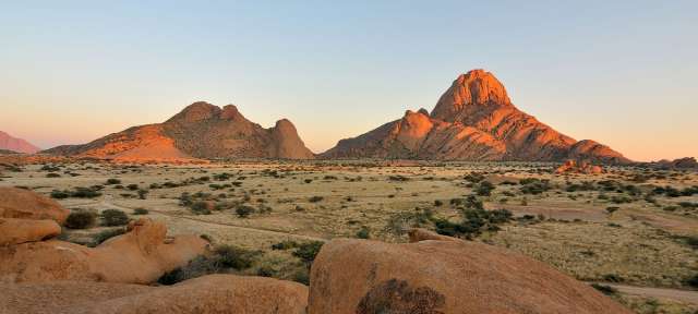 Sonnenaufgang in Spitzkoppe Ein großer Felsen in der Mitte einer Wüste mit Bergen im Hintergrund