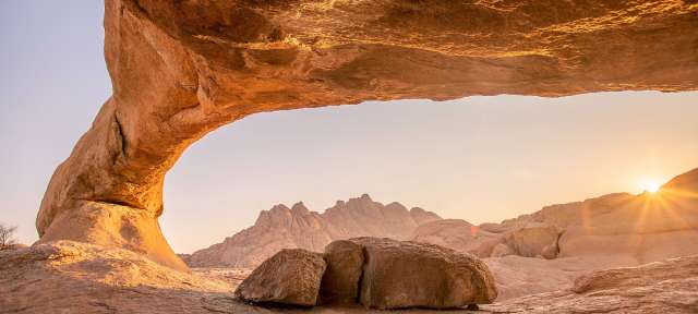 Spitzkoppe bei Sonnenaufgang Die Sonne scheint durch eine Felsformation in der Wüste