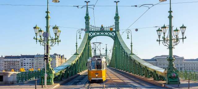 Eine gelbe Straßenbahn fährt über eine grüne Brücke