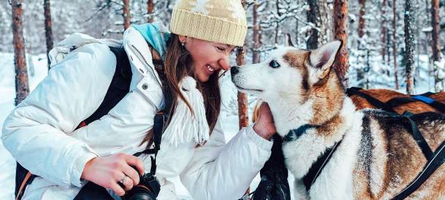Eine Frau hält eine Kamera und streichelt einen Husky-Hund im Schnee