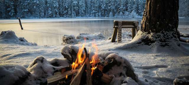 Ein Feuer brennt im Schnee neben einem zugefrorenen See