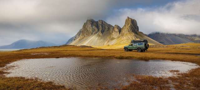 Ein grüner jeep steht neben einem kleinen teich mit einem berg im hintergrund