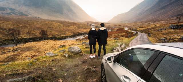 Ein Mann und eine Frau stehen neben einem Auto und schauen auf die Berge