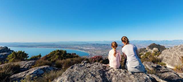 Eine Frau und ein Kind sitzen auf einem Felsen mit Blick auf einen See
