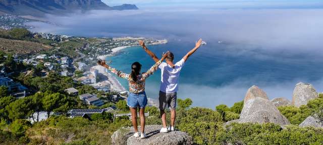 Blick vom Aussichtspunkt The Rock in Kapstadt über Campsbay Ein Mann und eine Frau stehen auf einem Felsen mit ihren Armen in der Luft