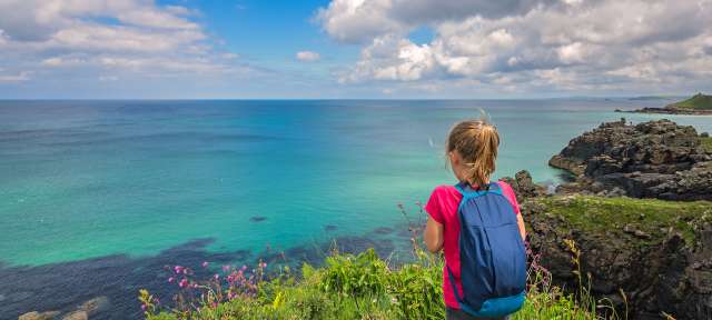 Ein kleines Mädchen mit einem blauen Rucksack schaut auf das Meer