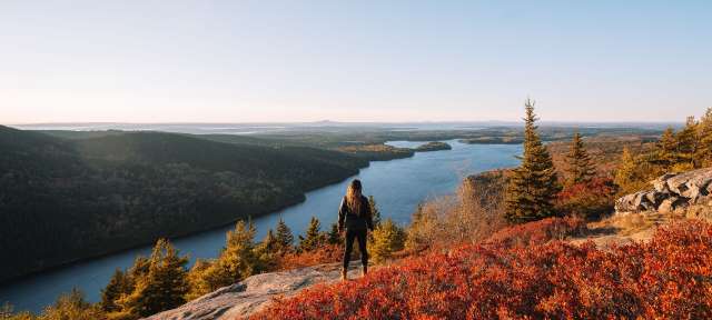 Acadia National Park Eine Frau steht auf einem Felsen mit Blick auf einen See