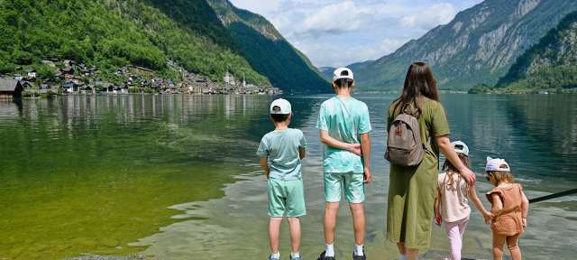 Eine Mutter mit vier Kindern steht am Ufer des Hallstätter Sees in Österreich und blickt auf die umliegende Berglandschaft.