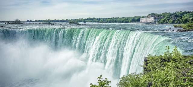 Grandioses Naturwunder: Niagara Fälle Ein Wasserfall mit einem Gebäude im Hintergrund