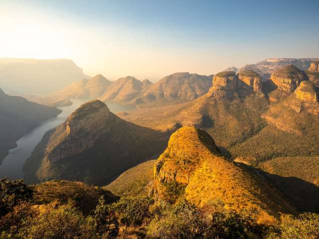 Eine weite Panoramaaufnahme der Blyde River Canyon Formationen im goldenen Licht der aufgehenden Sonne.