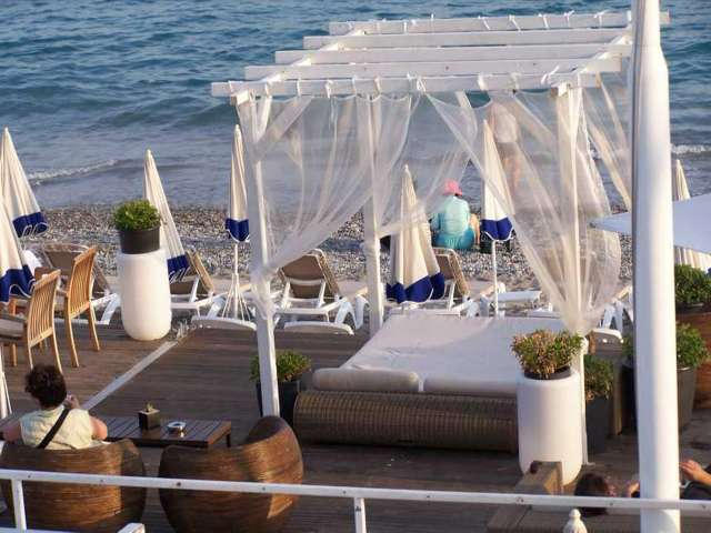 Das Bild zeigt einen Liegebereich am Strand mit zwei Personen, die auf Rattansesseln sitzen.
